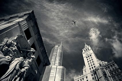 air plane flying over concrete buildings and statues in grayscale photography