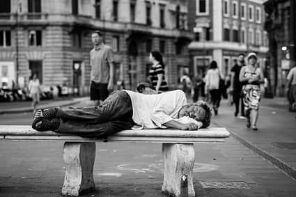 man sleeping on bench in the middle of the street